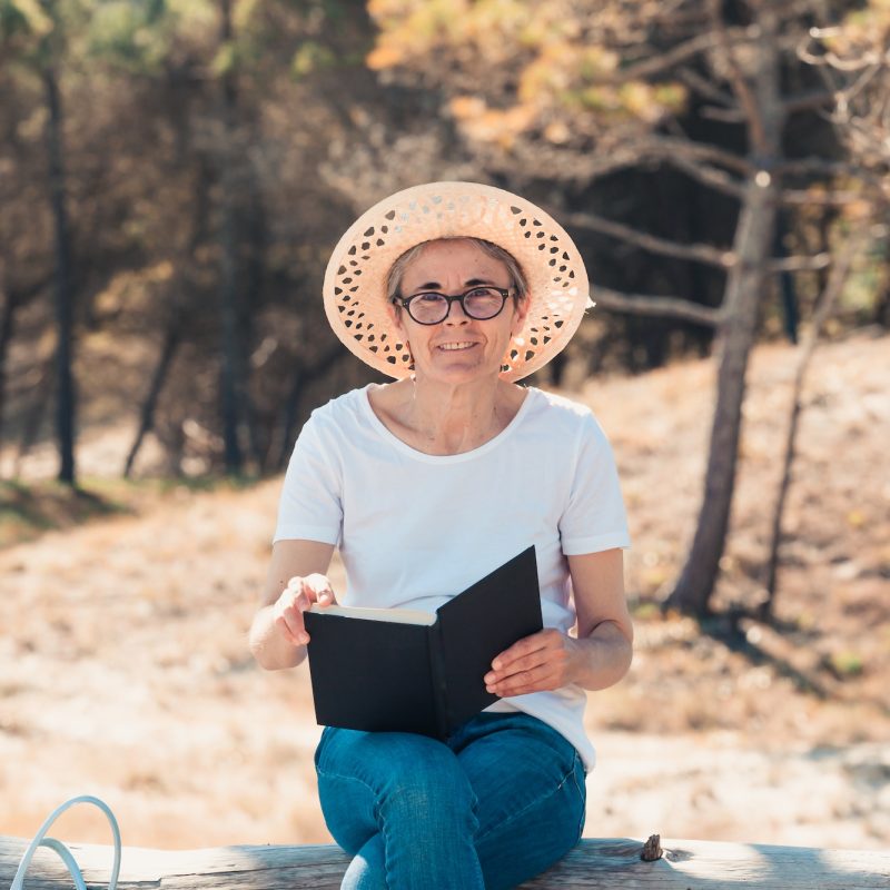 Old woman reading a book at the beach during a super sunny day. Freedom concept
